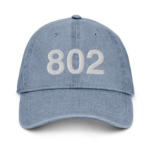 May include: A blue denim baseball cap with white embroidered text that reads "802".