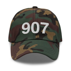 May include: Camouflage baseball cap with white embroidered text "907" on the front.