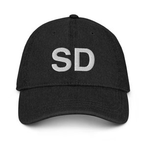 Peut inclure: Une casquette de baseball en denim noir avec les lettres "SD" brodées en blanc sur le devant.