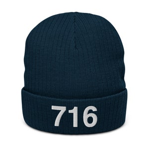 Op de afbeelding: Een donkerblauwe gebreide beanie met een wit geborduurd nummer "716" op de boord.