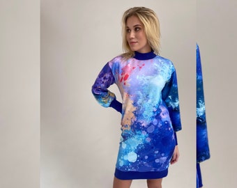 May include: A blue, pink and white abstract print dress with a high neck and long sleeves. The dress has a loose fit and a slightly gathered waist.