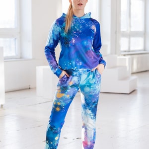 May include: A blue and purple hooded sweatshirt and matching sweatpants with a paint splatter design. The clothing is made of a soft, comfortable material.