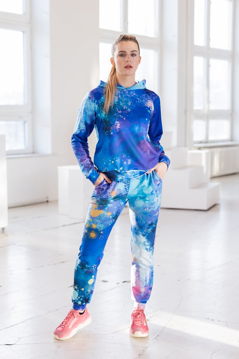 May include: A blue and purple hooded sweatshirt and matching sweatpants with a paint splatter design. The clothing is made of a soft, comfortable material.