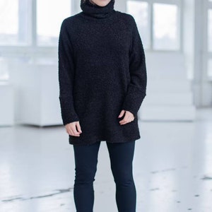 Könnte beinhalten: Eine Frau trägt einen schwarzen Rollkragenpullover und schwarze Leggings mit schwarzen Combat Boots. Der Pullover ist locker geschnitten und hat eine strukturierte Oberfläche. Der Text "SUSTAINABLE FABRIC" ist am unteren Rand des Bildes sichtbar.