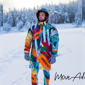 May include: A person wearing a colorful, abstract patterned winter jacket with the text "Move Addict" on the sleeve. The jacket is worn over orange and black patterned leggings. The person is standing in a snowy landscape.