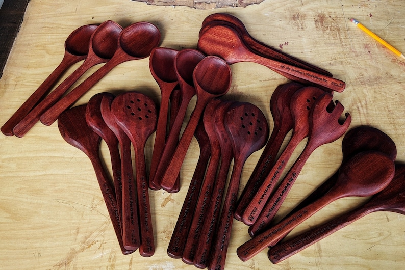 Puede incluir: Una colecci&oacute;n de cucharas de madera, esp&aacute;tulas y utensilios de servicio de color caoba rojo oscuro. Cada utensilio tiene un dise&ntilde;o &uacute;nico y est&aacute; grabado con un mensaje personalizado.