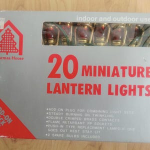 May include: A box of 20 miniature lantern lights for indoor and outdoor use. The box is gray with red and white text and graphics, including the words "Christmas House." The lights are red and gold.
