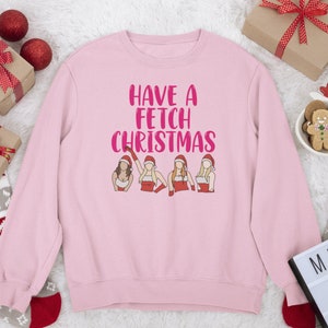 May include: Pink sweatshirt with the text "Have a Fetch Christmas" in pink lettering. Four female figures in Santa outfits are depicted below the text.