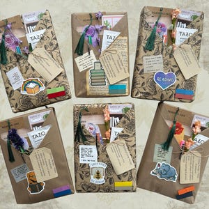 May include: An assortment of wrapped gifts, each adorned with decorative elements. The gifts are wrapped in brown paper with a floral pattern and embellished with stickers, tags, tassels, and flowers. Some gifts include Tazo tea packets and the word "Reading".
