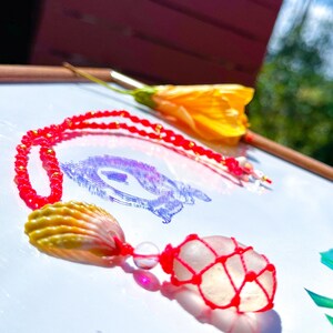 May include: A red beaded necklace with a white and pink seashell charm and a clear quartz crystal wrapped in red string.