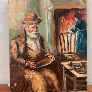 May include: Oil painting depicting an elderly man with a long white beard and a hat, seated indoors. He holds an object, possibly a loaf of bread. A woman in a blue dress tends to a fire in the background. The artwork is framed and mounted.