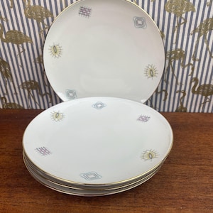 May include: Three white ceramic plates with a gold rim and a geometric design in shades of blue, yellow, and pink.