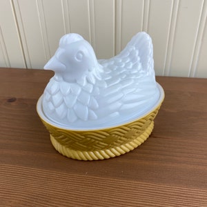 May include: White ceramic chicken shaped butter dish with a gold woven nest base.