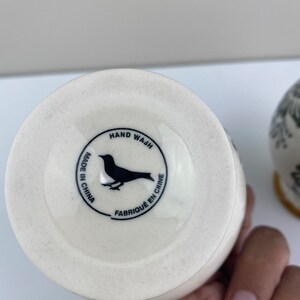 Może przedstawiać: Biały ceramiczny wazon z czarnym wzorem ptaka i tekstem "HAND WASH MADE IN CHINA FABRIQUE EN CHINE" na spodzie.