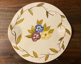 May include: A white oval serving platter with a green vine border and three painted flowers in shades of blue, yellow, and purple. The flowers are stylized pansies.