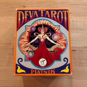 Könnte beinhalten: Eine Schachtel für ein Deva Tarot Deck mit einer farbenfrohen Illustration einer Frau in einem roten Kleid mit einer Krone und einem Pferdelogo. Der Text auf der Schachtel lautet "Deva Tarot" und "Piatnik".