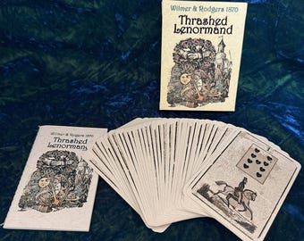 May include: A deck of Thrashed Lenormand cards by Wilmer & Rodgers 1870. The deck is fanned out, with two boxes and a card visible. The cards have illustrations of figures, symbols, and scenes. The box and cards are off-white with black and sepia-toned illustrations.
