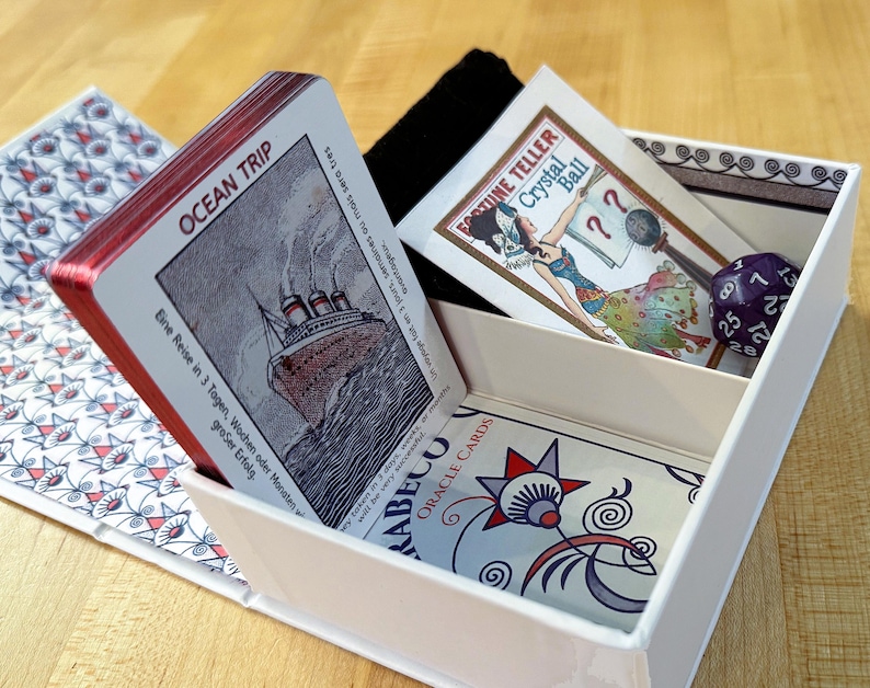 May include: A white box with a red and white deck of oracle cards inside. The box has a black fabric pouch and a card with a fortune teller illustration. The text on the card reads "Fortune Teller Crystal Ball". The text on the oracle cards reads "Rabecou Oracle Cards".
