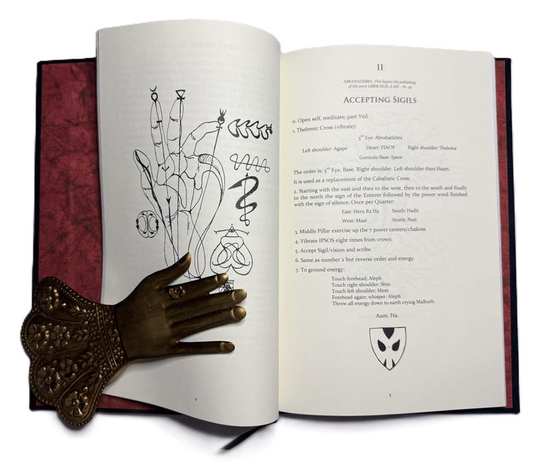 May include: An open book with illustrations and text, featuring a bronze hand-shaped bookmark. The book's pages display drawings of hands and symbols, with the title "ACCEPTING SIGILS" visible.