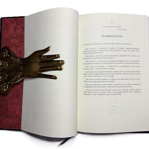 May include: An open book with a decorative brass hand bookmark. The bookmark is shaped like a hand with intricate floral details. The book has a red spine and the text "INTRODUCTION" is visible.