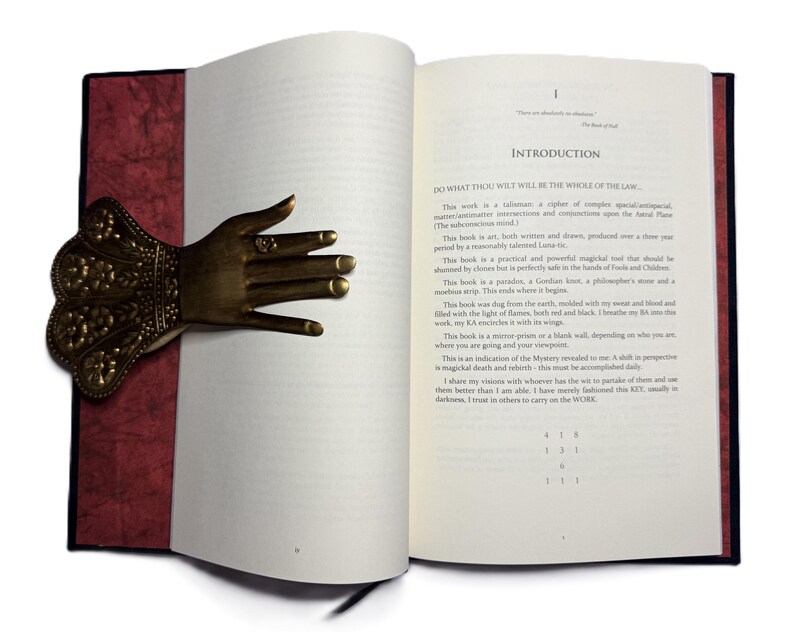 May include: An open book with a decorative brass hand bookmark. The bookmark is shaped like a hand with intricate floral details. The book has a red spine and the text "INTRODUCTION" is visible.