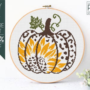 May include: Cross-stitch pattern of a pumpkin with a sunflower design. The pumpkin is brown with white and yellow accents. The pattern is in a wooden embroidery hoop.