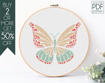 May include: A cross-stitch pattern of a butterfly with peach, coral, and green wings. The pattern is displayed in a wooden embroidery hoop.