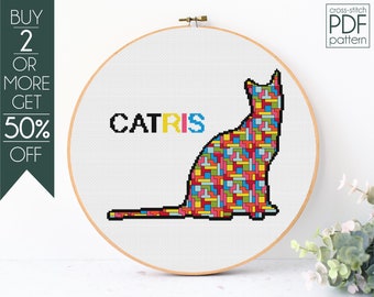 May include: Cross-stitch pattern featuring a colorful cat silhouette with the word "CATRIS" in rainbow colors. The pattern is displayed in a wooden embroidery hoop.