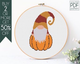 May include: Cross-stitch pattern of a gnome sitting on a pumpkin. The gnome is wearing a brown and red hat with a curled brim, a brown beard, and a white shirt. The pumpkin is orange.