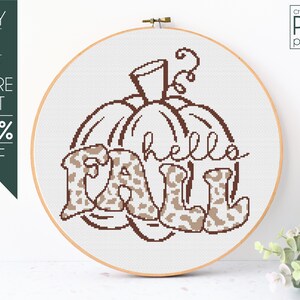 May include: Cross-stitch pattern featuring a brown outline of a pumpkin with the word "hello" and the word "fall" in brown with a leopard print pattern.