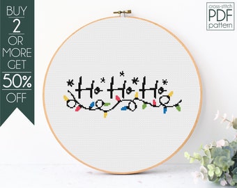 Op de afbeelding: Een kruissteekpatroon met de tekst "Ho Ho Ho" met kleurrijke lichtslingers. Het patroon wordt weergegeven in een houten borduurring.