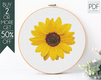 May include: Cross-stitch PDF pattern of a sunflower in a wooden embroidery hoop. The sunflower is rendered in shades of yellow and brown, with a detailed pixelated design. The text "cross-stitch PDF pattern" is visible.