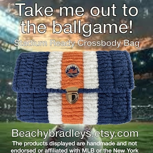 May include: A blue, white, and orange crossbody bag with a Mets logo. The bag has a gold clasp and is made of a textured material. Text on the bag reads "Take me out to the ballgame!" and "Stadium Ready Crossbody Bag."