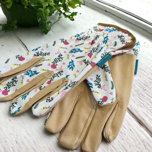 May include: A pair of gardening gloves with a floral print. The gloves are white with pink, blue, and yellow flowers and leaves. The palms of the gloves are a light brown color.