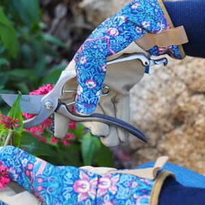 May include: A pair of blue and pink floral gardening gloves with a pair of pruning shears. The shears have a silver blade with the text "M&F" on the blade.