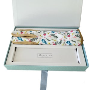 May include: A light blue gift box with a white ribbon and a pair of gardening gloves with a floral print inside. The box has the text "Moor & Fen" on the inside.