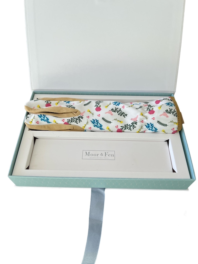 May include: A light blue gift box with a white ribbon and a pair of gardening gloves with a floral print inside. The box has the text "Moor & Fen" on the inside.