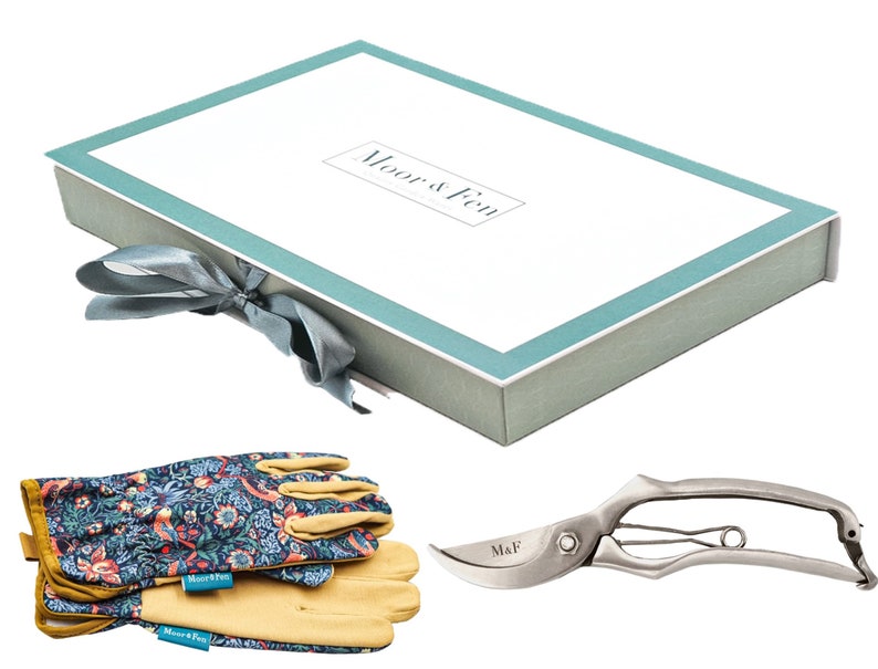 May include: A gardening gift set in a light blue and white box with a gray ribbon. The set includes a pair of floral patterned gardening gloves and a pair of silver pruning shears with the text "M&F" on the handle.