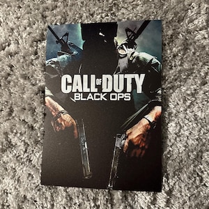 Op de afbeelding: Een zwarte en groene videogamehoes met de tekst "Call of Duty Black Ops" in wit. Een soldaat houdt twee wapens voor zich.