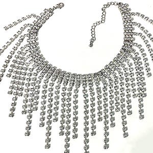 May include: A silver-toned necklace with a cascading fringe design. The necklace features multiple strands of small, square-cut rhinestones that hang down from a curved base. The necklace has an adjustable chain closure.