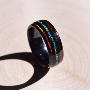 May include: A black ceramic ring with two bands of brown wood and a band of iridescent opal inlay.