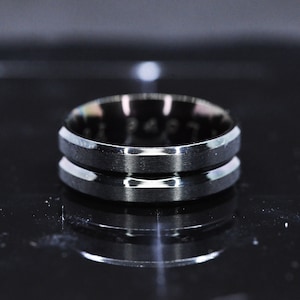 May include: A silver ring with a beveled edge and a grooved design.