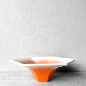 May include: A hexagonal bowl featuring a gradient color scheme that transitions from a bright orange base to a white rim. The bowl has a wide, flared opening with flat, angled sides that taper down to a smaller, solid orange hexagonal pedestal base.