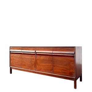 May include: A long, rectangular wooden sideboard featuring a rich, dark brown wood grain finish. The piece includes four cabinet doors with integrated horizontal handles and a matching row of four drawers positioned directly above the doors.
