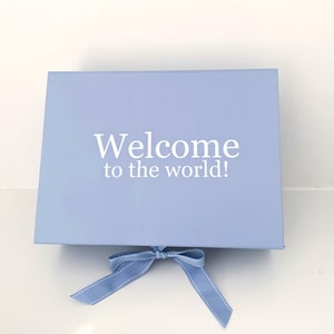 May include: A pale blue gift box with a matching ribbon bow. The box lid displays the white text "Welcome to the world!". This box is suitable for a baby shower or a newborn gift.