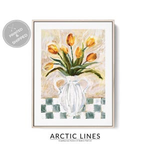 May include: A framed art print depicting a still life of yellow tulips in a white vase with handles. The vase is on a checkered surface. The background is a textured, off-white colour. The text "ARCTIC LINES" is at the bottom.
