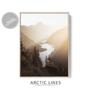 May include: A framed print of a mountain landscape with a river running through a valley. The image is illuminated by sunlight, creating a hazy effect. The print is labelled "Arctic Lines" and "Scandinavian Posters & Modern Wall Art."