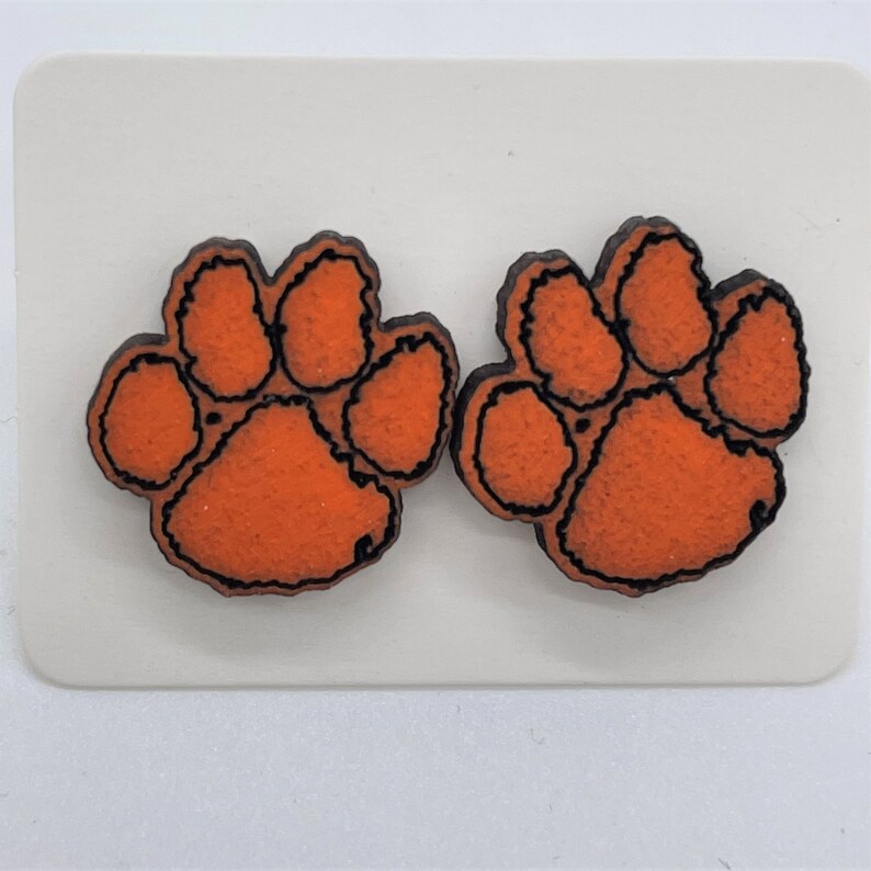 May include: A pair of orange and black paw print earrings. The paw prints are outlined in black and have a textured surface.