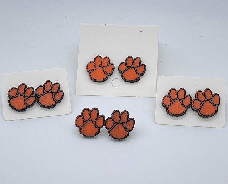 May include: Three sets of orange and black paw print earrings. Each set has two earrings.