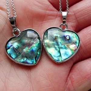 May include: Two heart-shaped pendants with iridescent abalone shells set in silver-toned metal. Each pendant hangs from a delicate silver chain. The abalone shells display a range of colors, including blues, greens, and purples.
